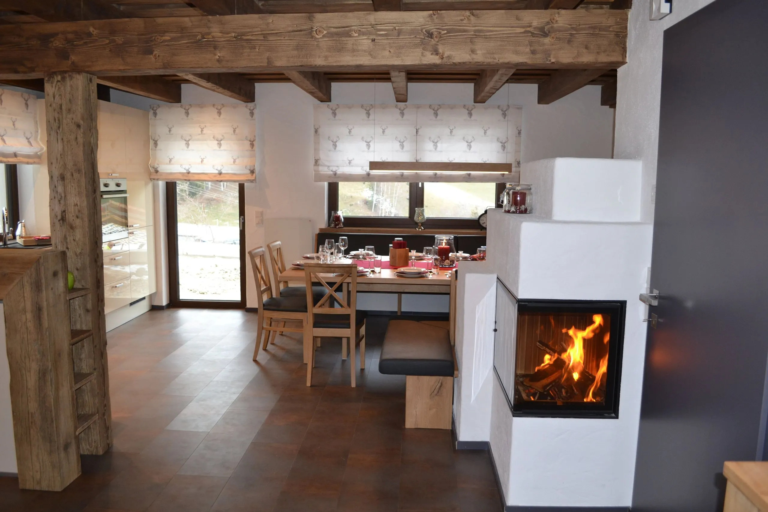 Wohnbereich im Comfort Chalet Bergzeit mit weißem Kaminofen und Esstisch am Fenster