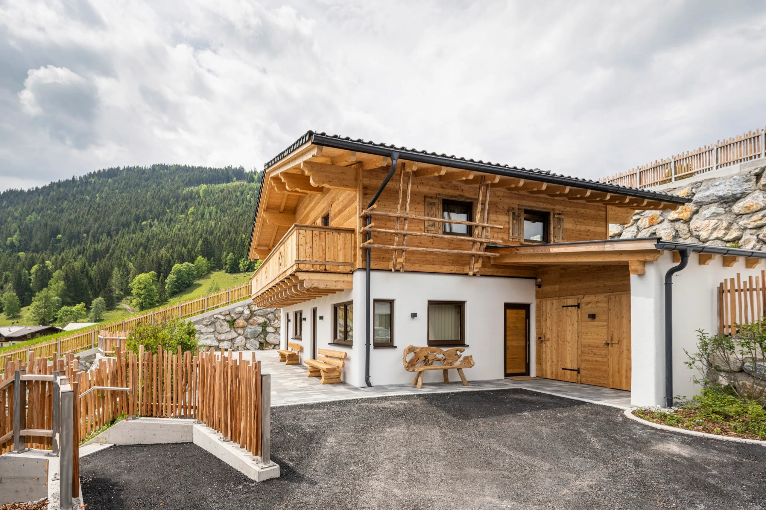 Chalet mit Zufahrt und Holzzaun an einem Sommertag