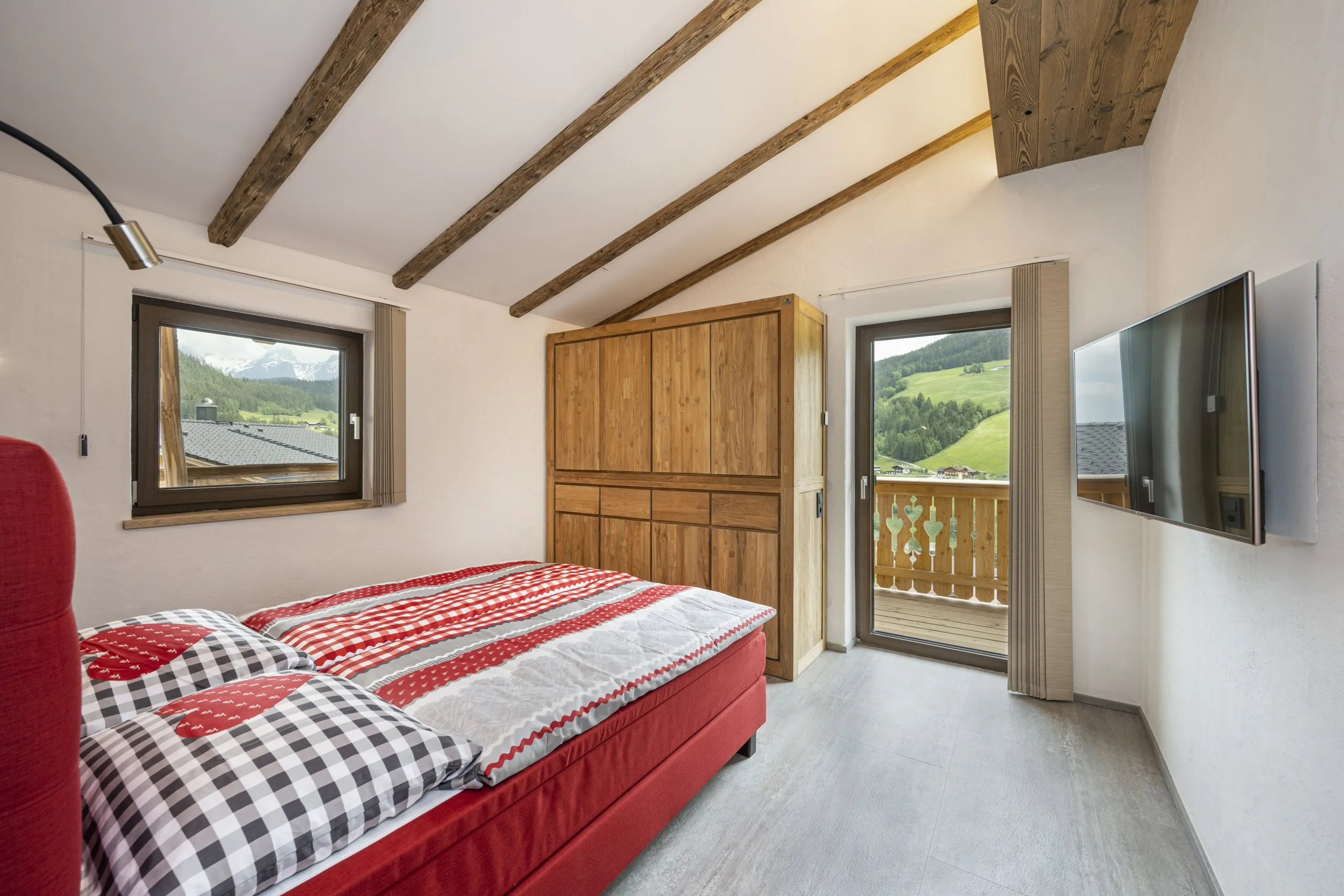 Doppelzimmer mit rot karierter Bettwäsche, Fernseher und Tür zum Balkon