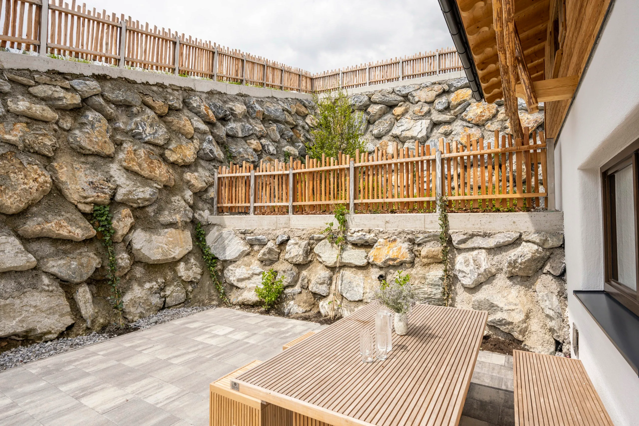 Terrasse mit Holzmöbeln vor einer Natursteinmauer
