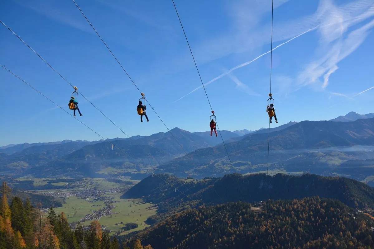 Vier Zipline-Fahrer hoch über einem Tal mit Bergpanorama
